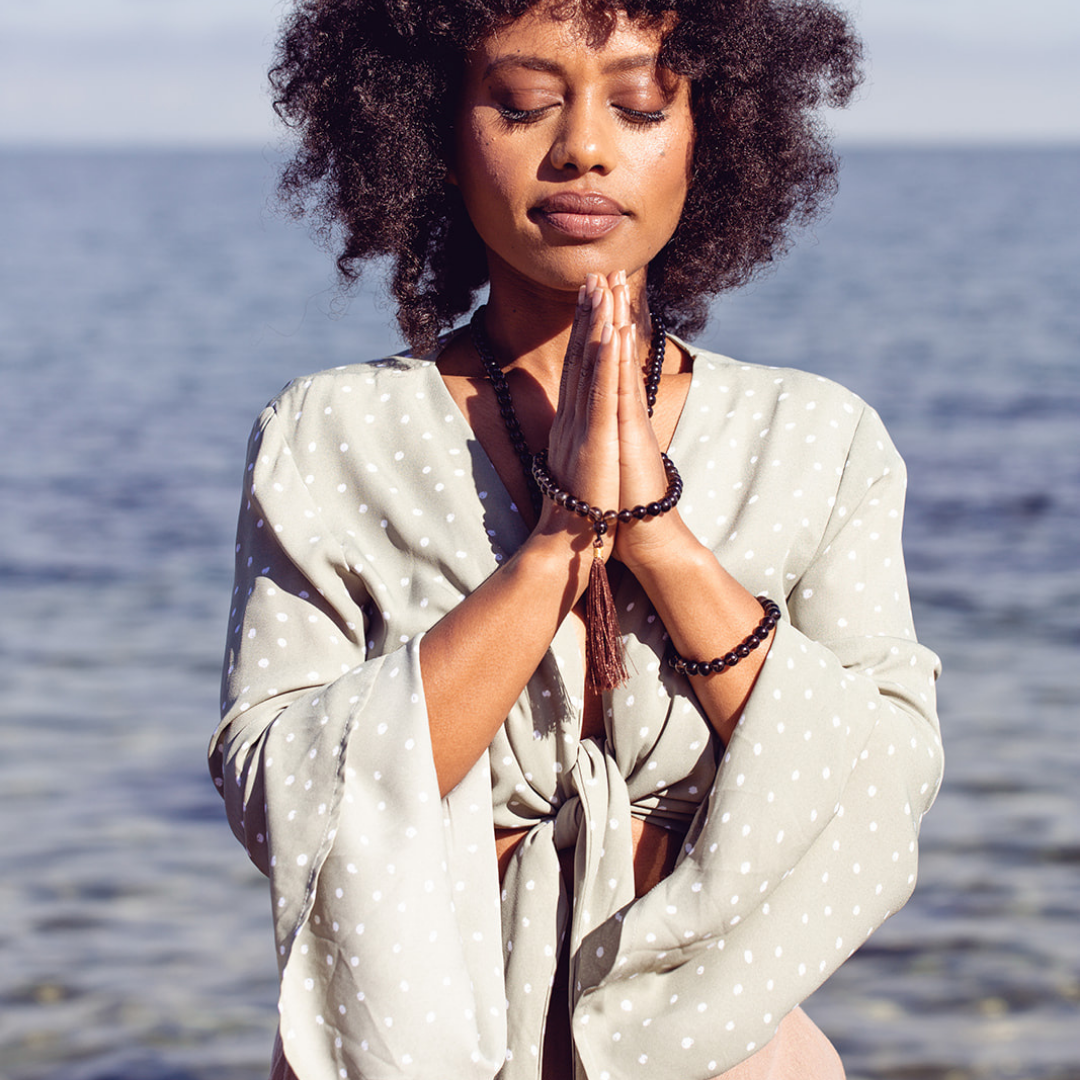 Woman with eyes close in prayer wih water in the background wearing Ambarya Release - Smoky Quartz Mala Bead Set