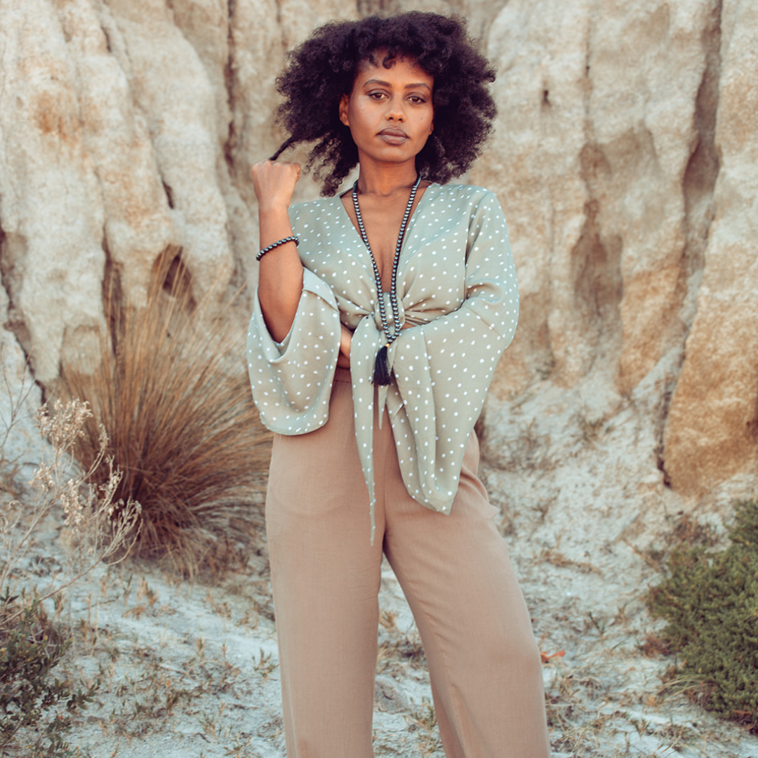 Woman standing against a sandy background, looking at the camera wearing Ambarya Strength - Hematite Mala Bead Set