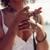 Close up of woman wearing Ambarya Good health - Bloodstone Mala Bead Set. She is holding the beads in her hand
