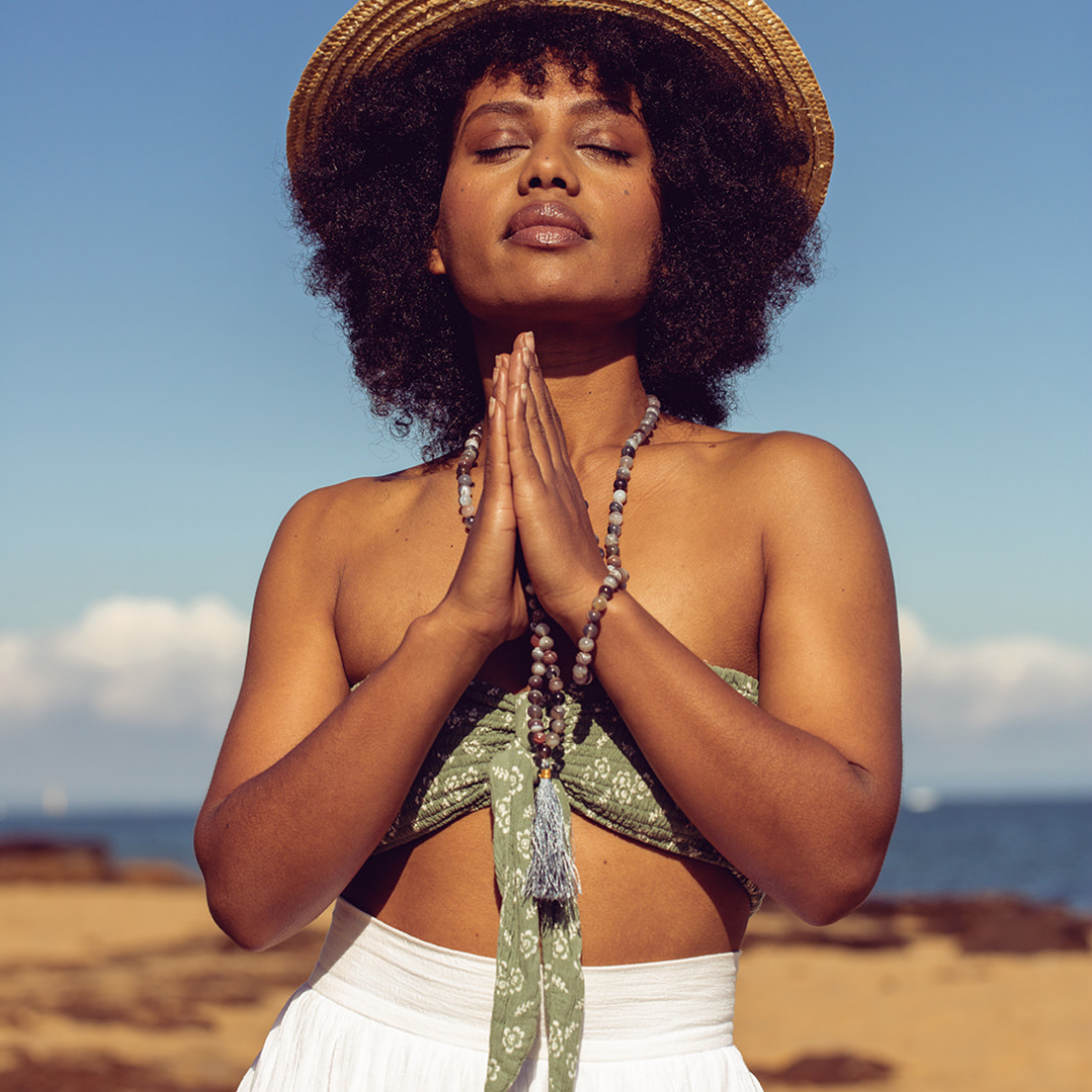 Woman standing with eyes closed and hands in prayer position wearing Ambarya Acceptance - Botswana Agate Mala Bead Set