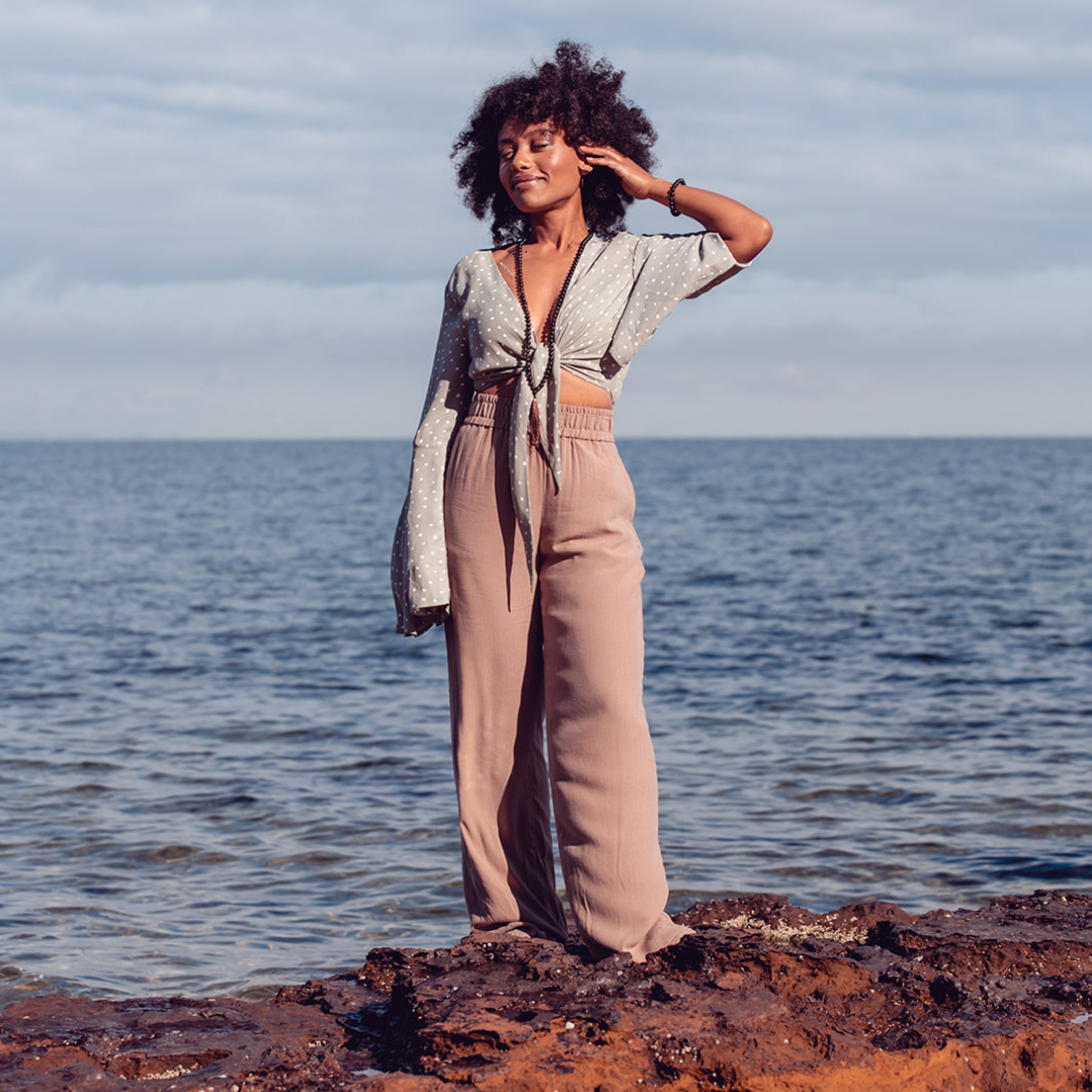 Woman smiling and standing on rocks near water wearing Ambarya Release - Smoky Quartz Mala Bead Set